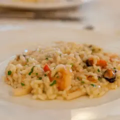 Szybkie risotto z warzywami i owocami morza, posypane natką pietruszki, na białym talerzu.