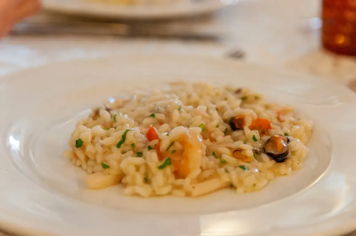Szybkie risotto z warzywami i owocami morza, posypane natką pietruszki, na białym talerzu.