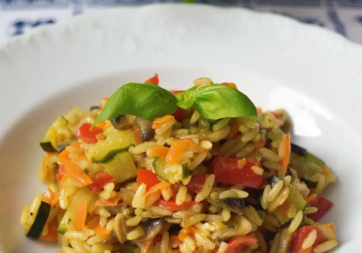 Szybkie risotto z warzywami: ryż z cukinią, papryką, marchewką i pieczarkami, ozdobione listkiem bazylii.